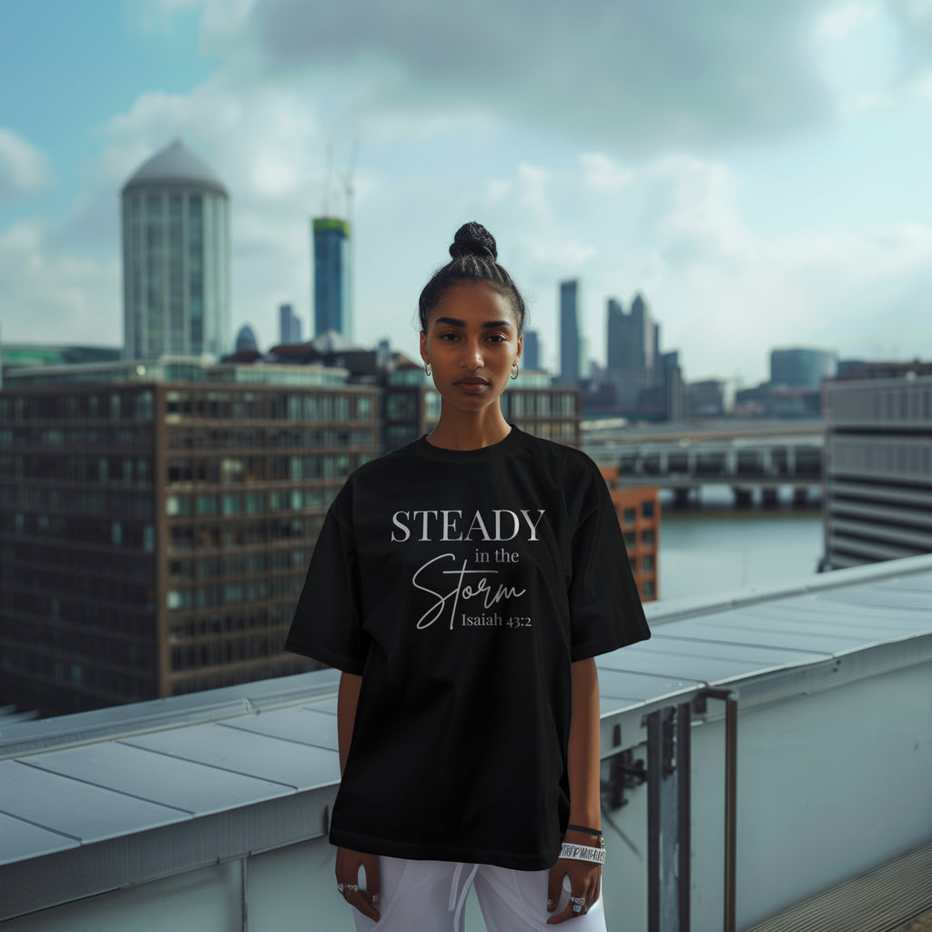 Female model wearing a black women’s Christian t-shirt front view featuring the phrase “STEADY in the Storm Isaiah 43:2” with Storm written in a handwritten script font