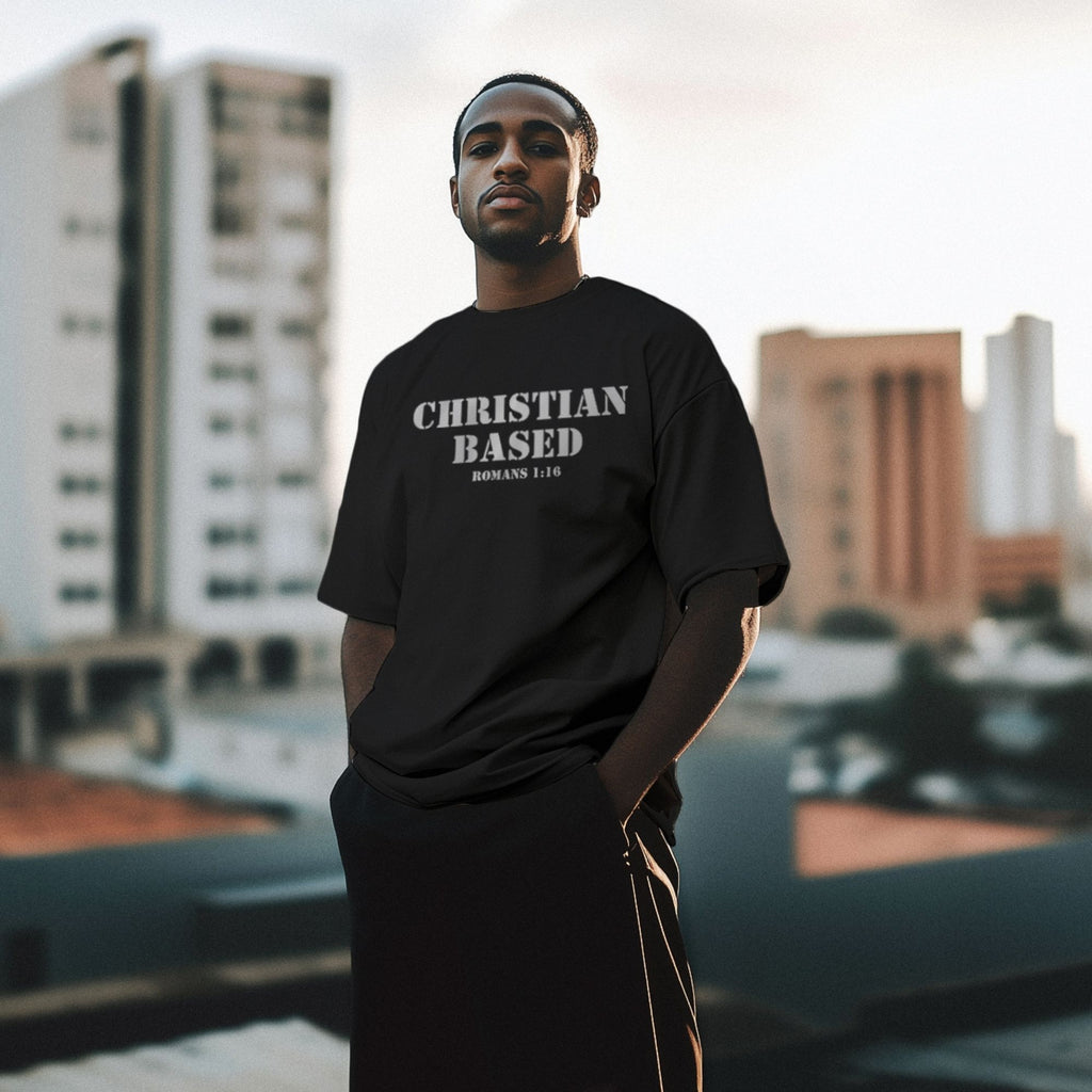 Male model wearing a black men’s Christian t-shirt front view featuring the text Christian Based and Romans 1:16 in a military stencil font
