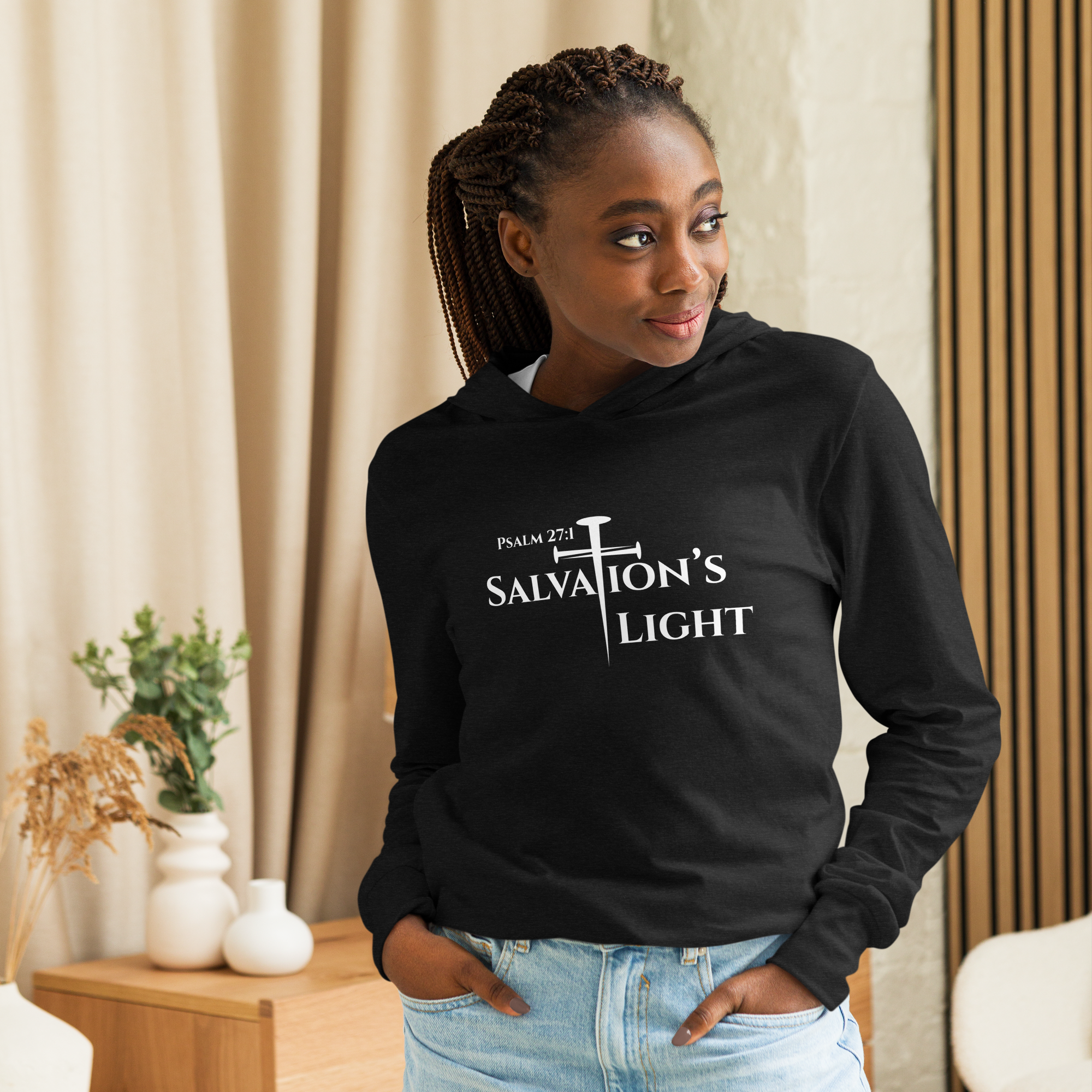 Female model wearing a black Salvation's Light Christian Long Sleeve Lightweight Hoodie from the Salvation’s Light Signature Collection, featuring Psalm 27:1 and the word “Salvation’s Light” with the T designed as a white three-nail cross