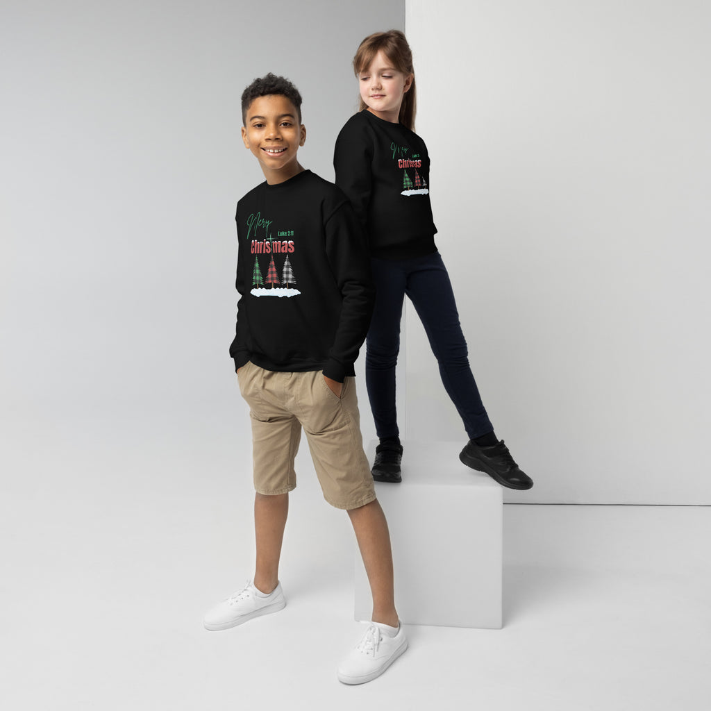 Boy and girl wearing black youth Christmas sweatshirts featuring buffalo plaid trees, snow on the ground, Merry Christmas text, Luke 2:11, and cross-shaped T design