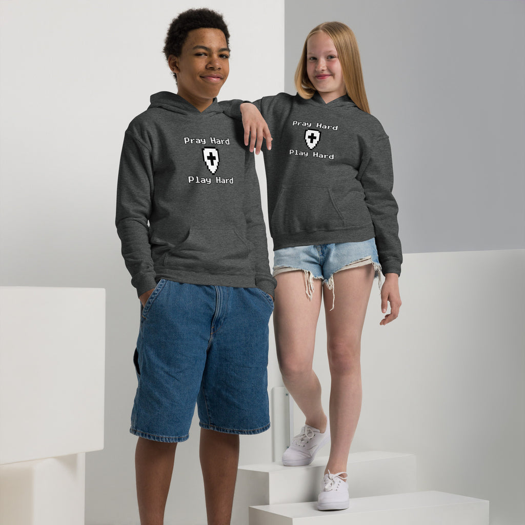 Boy and girl wearing a kids Christian hoodie in dark heather showing the front design text “Pray Hard” above a shield with a cross and the text “Play Hard” below in a gamer pixel font
