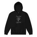 Flat lay front view of a girls Christian hoodie in black featuring the exact text “Pray Hard” and “Slay Hard” in script font with a heart and a cross in the center between the phrases