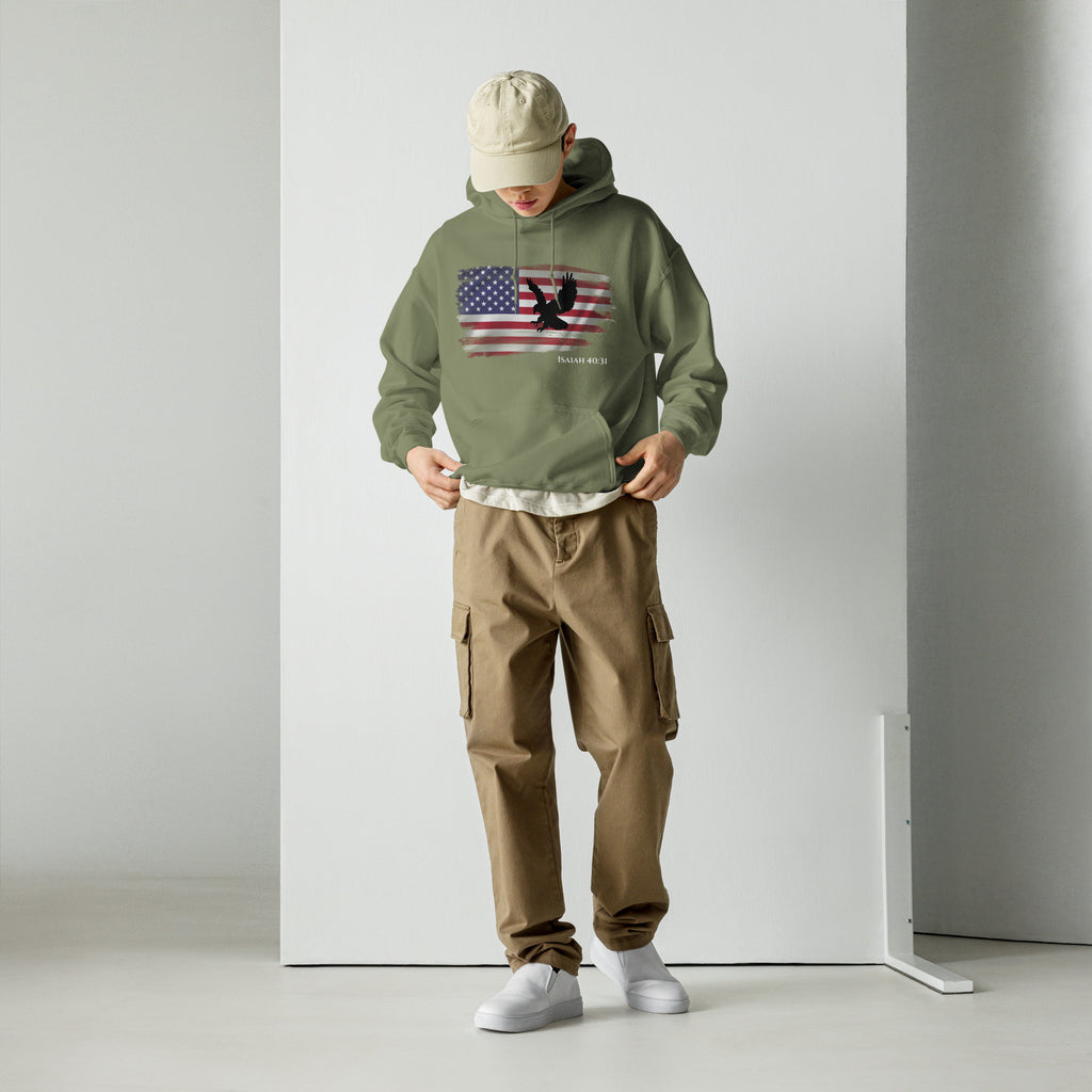 Male model wearing a military green men’s Christian patriotic hoodie showing the front design with a distressed American flag, black flying eagle, and the text “Isaiah 40:31.”