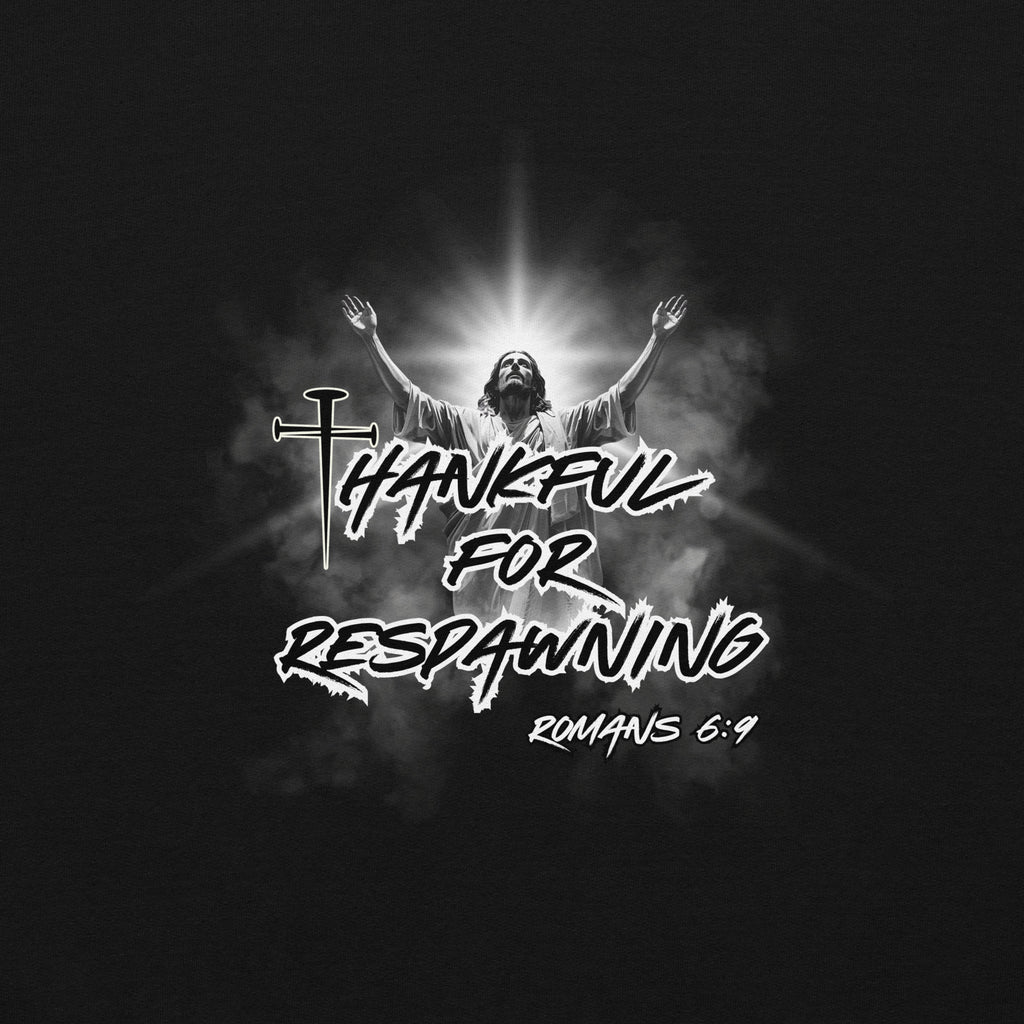 Close-up view of the black men’s Christian hoodie highlighting the full design text “Thankful for Respawning” and “Romans 6:9” in an urban style font, the “t” in Thankful formed by three nails, and Jesus looking to Heaven with His arms raised with light rays and clouds behind Him.