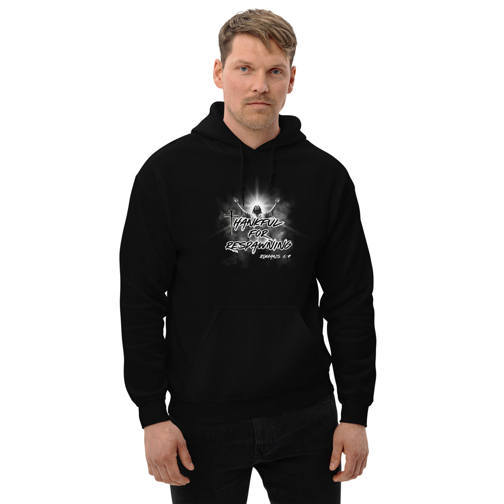 Male model wearing the black men’s Christian hoodie against a white brick wall, showing the front design with the full text “Thankful for Respawning” and “Romans 6:9,” the "t" in thankful is designed with a three-nail cross and Jesus with arms raised toward Heaven.
