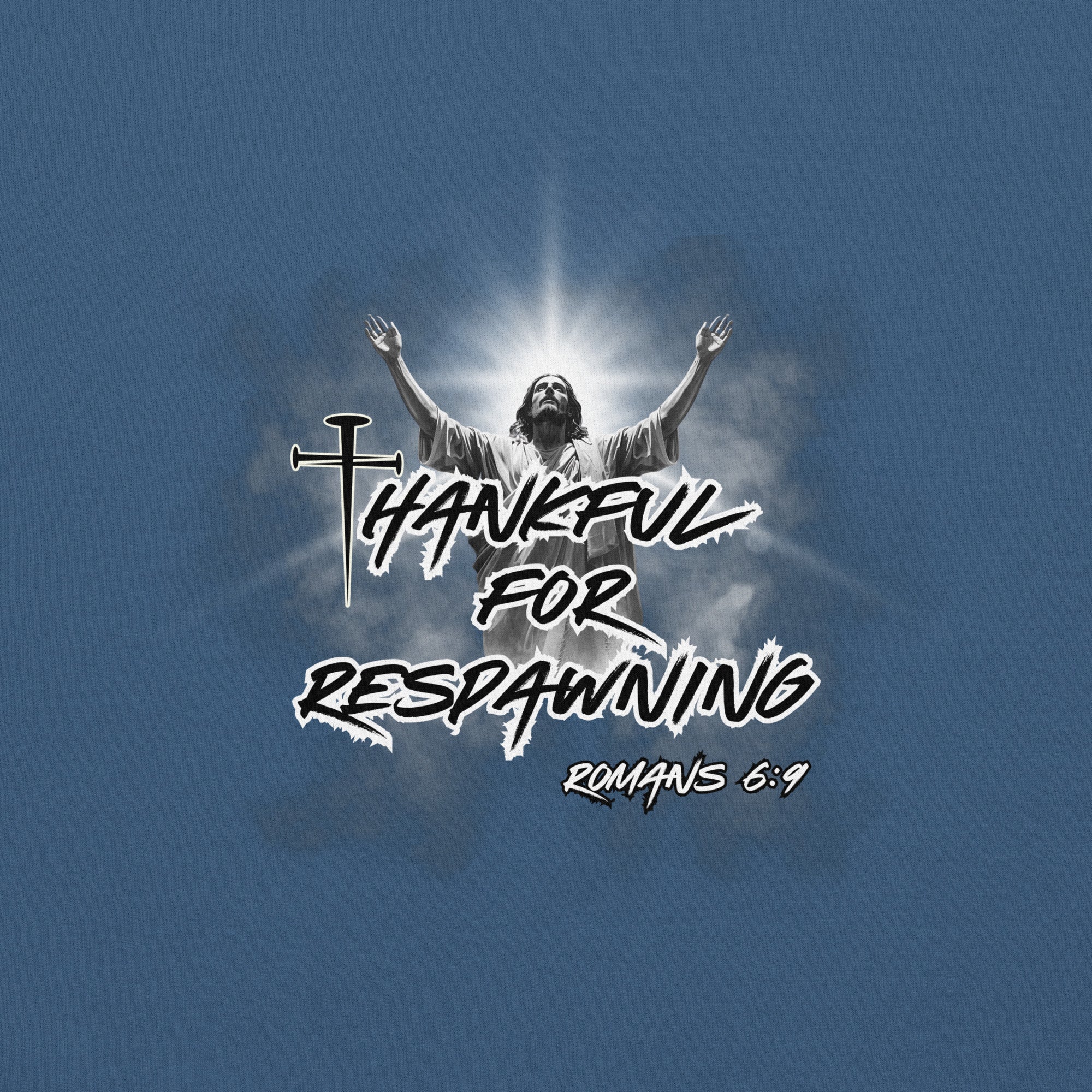 Close-up detail of the indigo blue men’s Christian hoodie showing the full design text “Thankful for Respawning” and “Romans 6:9,” the “t” in Thankful created with three nails, and Jesus looking to Heaven with His arms raised with light and clouds behind Him.
