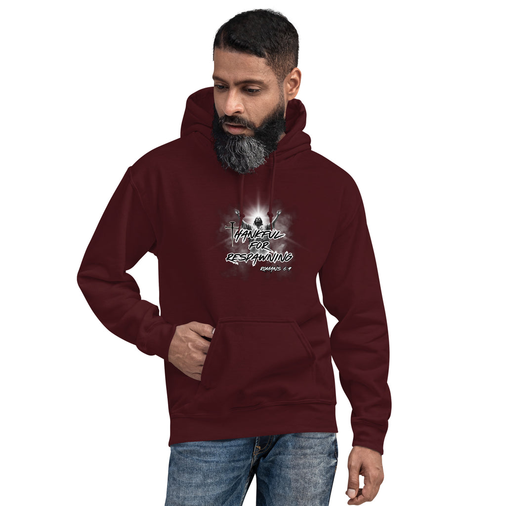 Male model wearing the maroon men’s Christian hoodie against a white brick wall, showing the front design with the full text “Thankful for Respawning” and “Romans 6:9,” the "t" in thankful is designed with a three-nail cross and Jesus with arms raised toward Heaven.