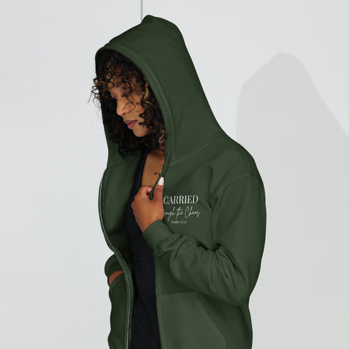 Female model wearing a forest green women’s zip hoodie with the left chest text “CARRIED through the Chaos Psalm 55:22.” “Through the Chaos” appears in a handwritten font.